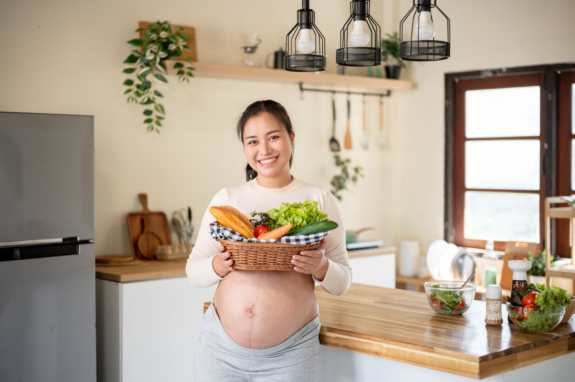 キッチンで食材を持つ笑顔の妊婦