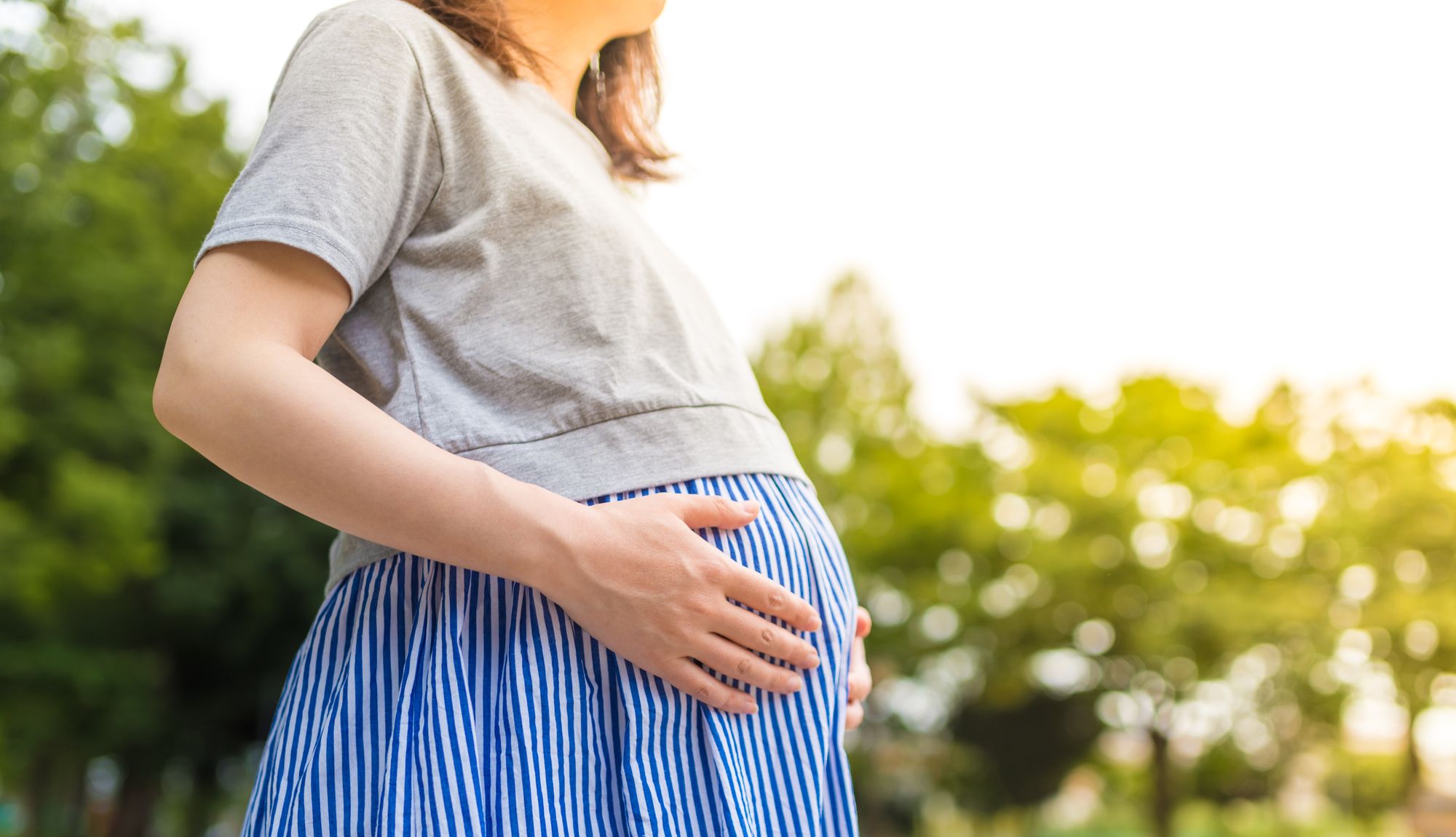 新緑の中でお腹を触る妊婦さん