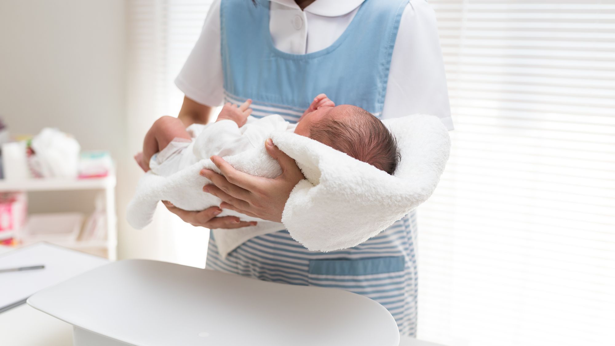 赤ちゃんを抱いて体重を測る助産師